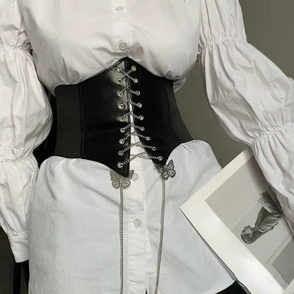 Corset Papillon en simili cuir noir avec laçage et chaînes papillon, porté sur une chemise blanche élégante.