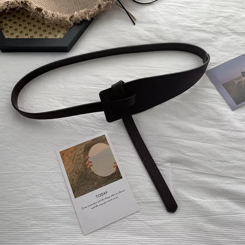 Ceinture Corset Cuir Noir elegante sur table en bois blanc avec carte postale et tissu beige texture